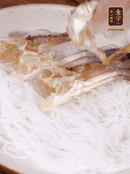 盤底墊上粉絲，擺上梭子蟹、火腿片，撒姜粒，淋上蒸魚豉油、花雕酒調味腌制15分鐘